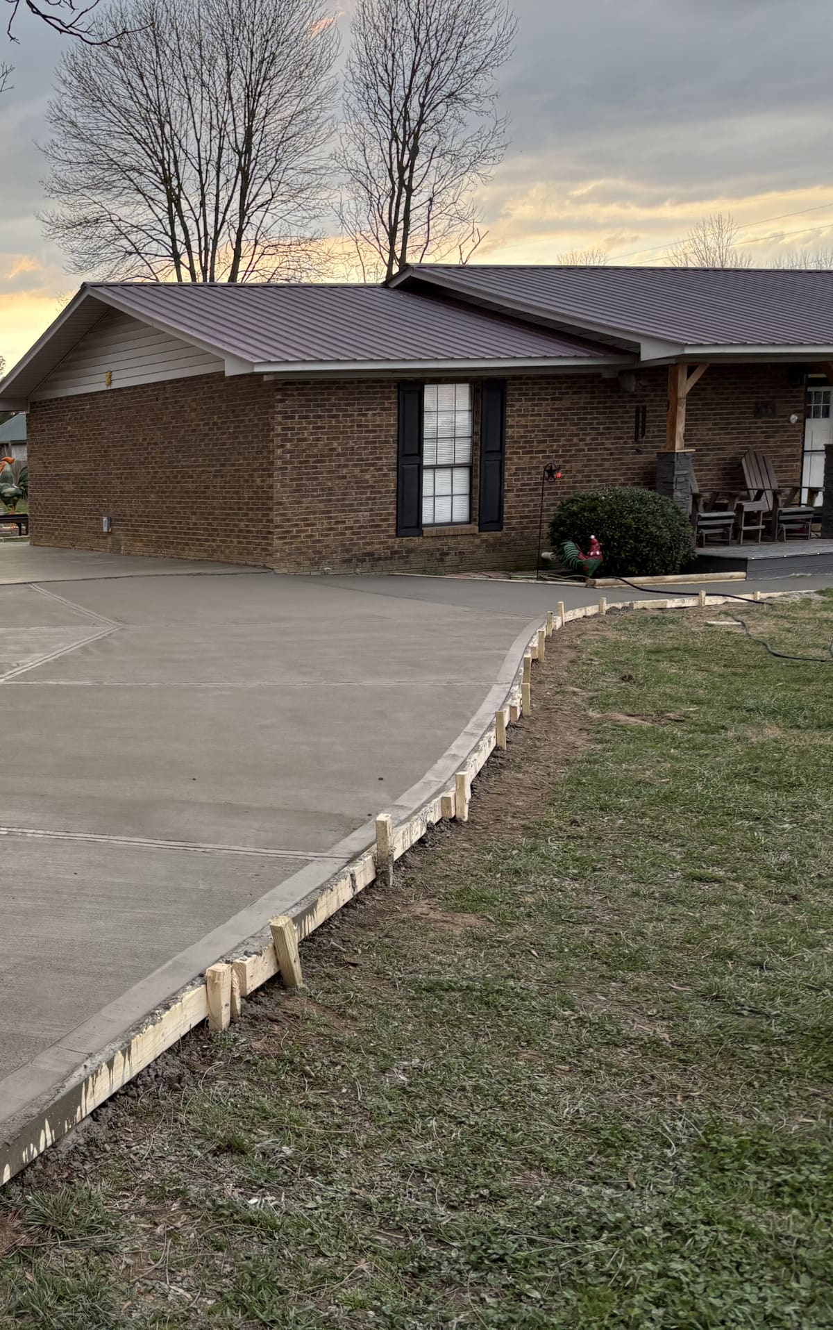 Fresh broom-finished driveway curving past a brick house with a metal roof and covered porch, wood forms along the edge