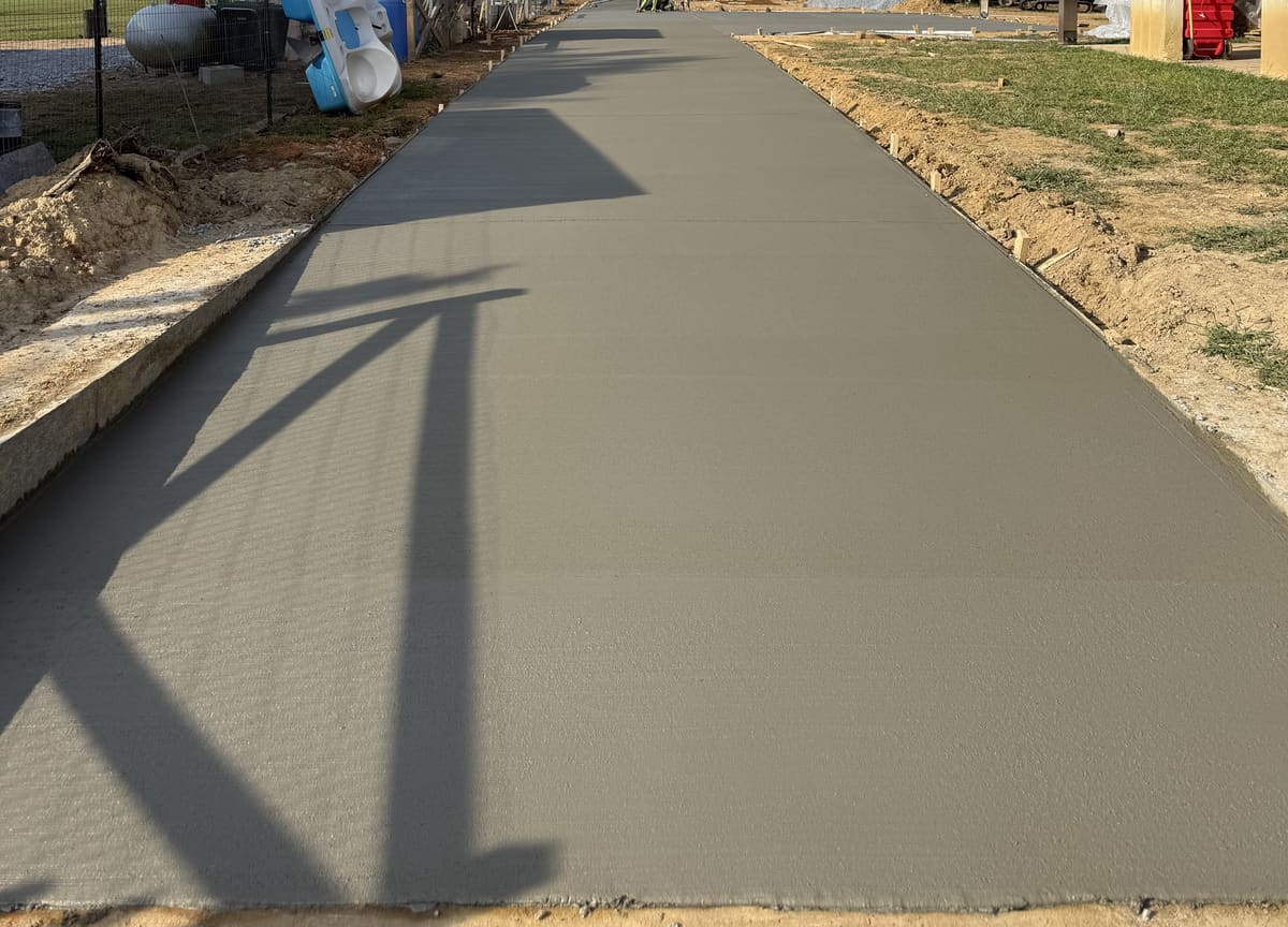 Long fresh broom-finished driveway striped with shadows, stakes and wood forms along its right edge