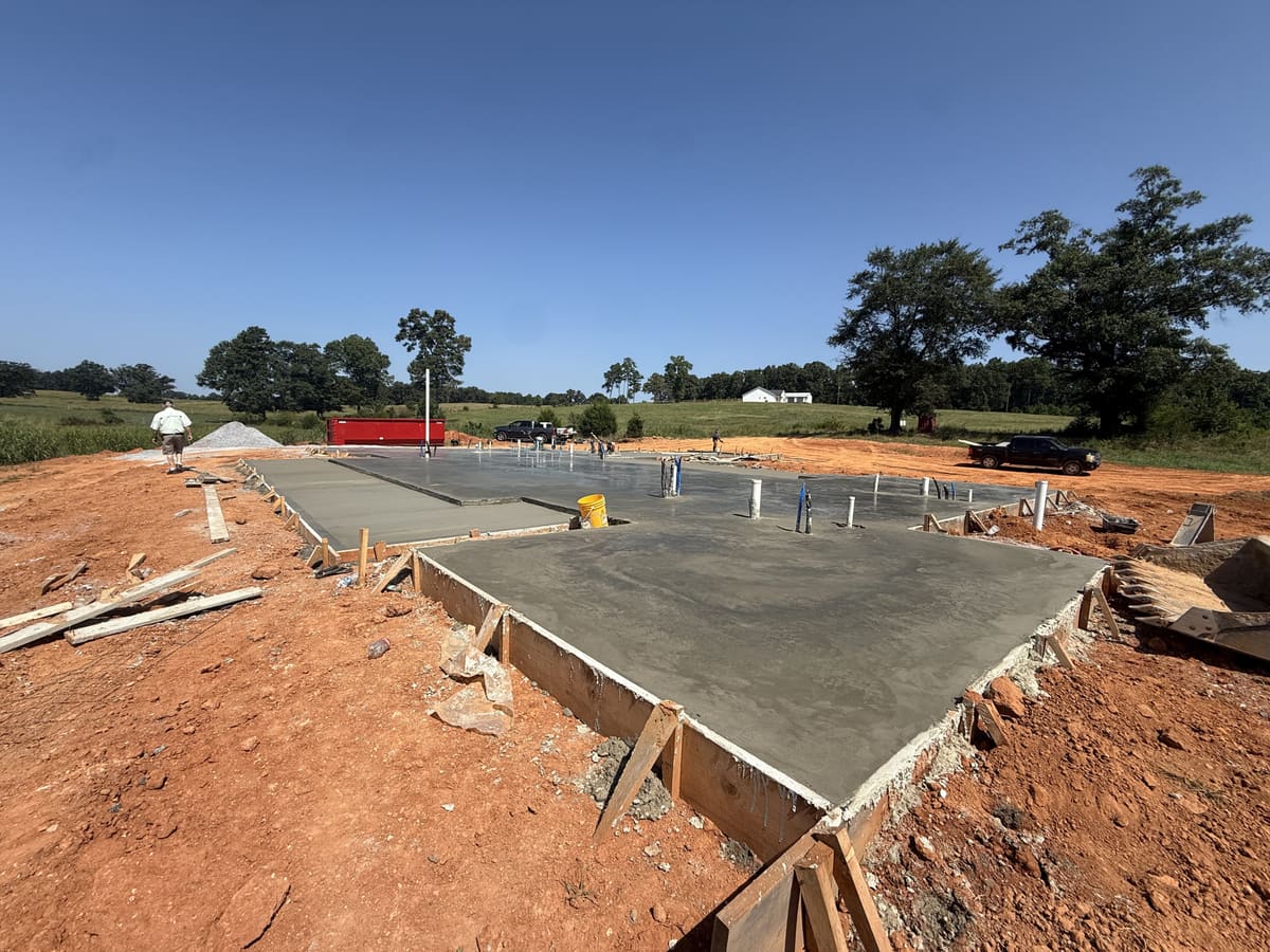 Fresh house slab with plumbing pipes rising through it, wood forms on the edges and red clay all around