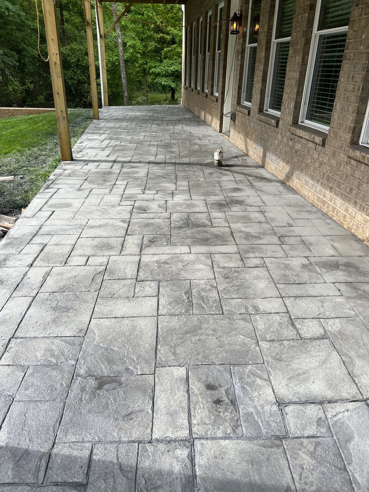 Gray stamped concrete in a stone tile pattern along a brick house under a covered porch