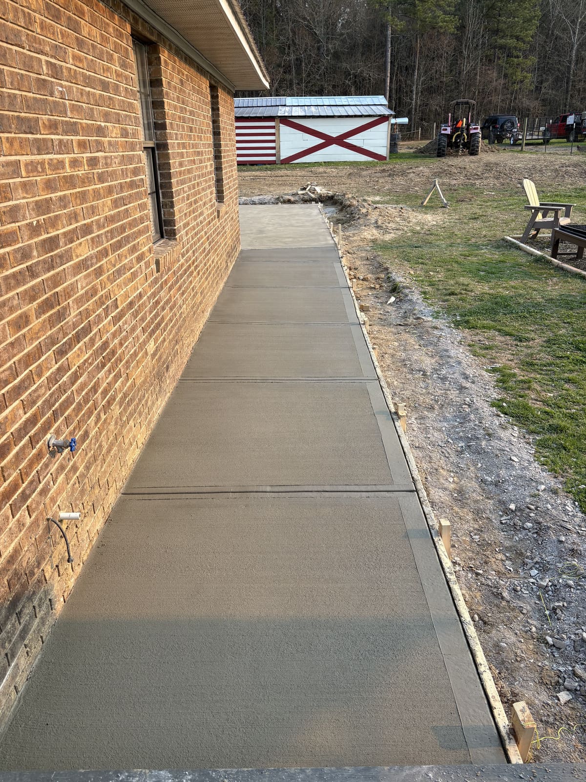 Fresh broom-finished walkway with control joints along a brick house wall, forms still on the outer edge